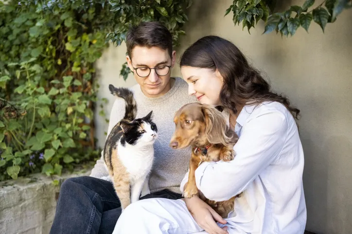 Young couple sitting in backyard holding a cat and a dog